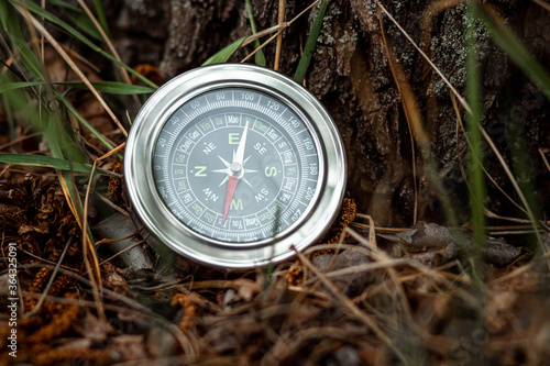 Magnetic silver compass on a background of greenery. The concept of travel, finding a way, vacation. Copy space.