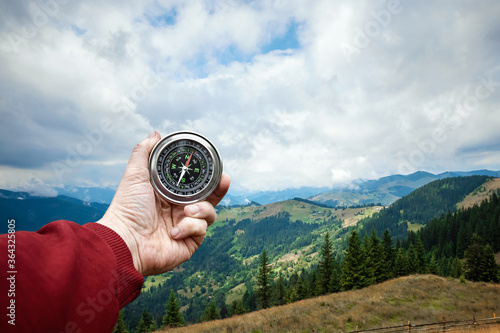 Close-up Male hand and silver compass on a background of mountain landscape. The concept of travel, hiking, help, searching, vacation. Copy space.