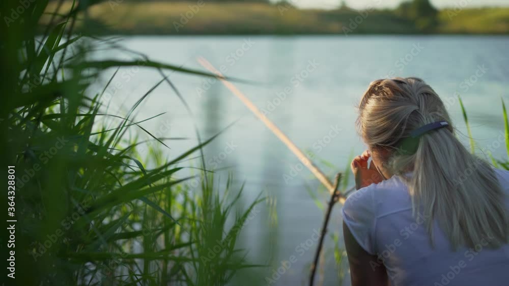 A young girl fishing, sitting on the shore with a fishing rod and waiting for a catch. Young girl fishing from a dock in a lake on a sunny day A young girl fishing, sitting on the shore with a fishing rod and waiting for a catch. Young girl fishing from a dock in a lake on a sunny day