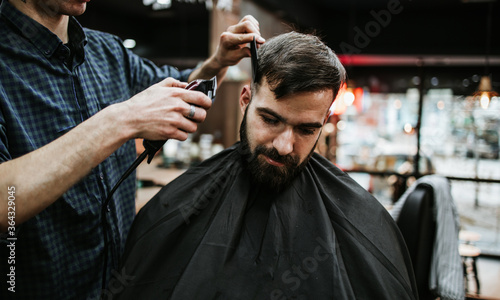 Good looking young adult man getting a hair and beard styling and dressing treatment by professional hairstylist.