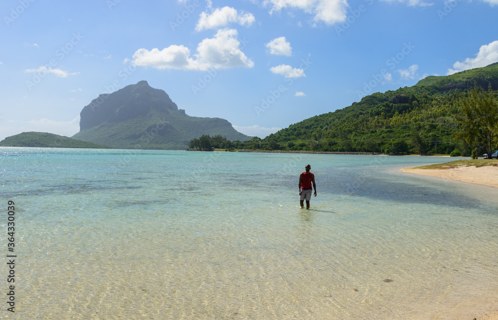 man walking on the beach with Le Morne mountain on the background
