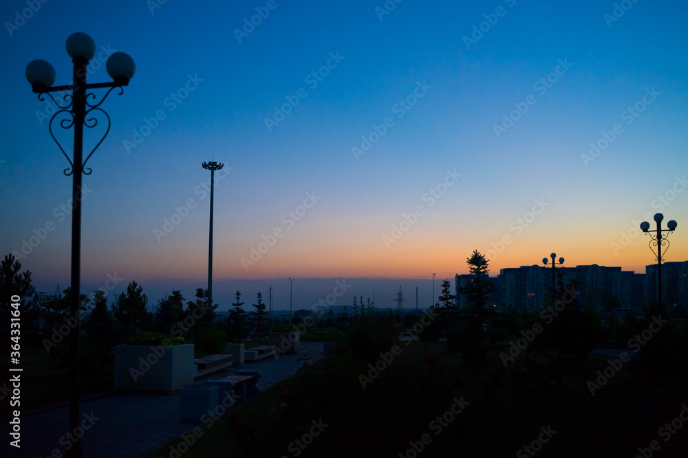Dawn in the city. The city before dawn. Silhouettes of lanterns. The sun rises. Bright streak in the sky. Dawn sky over tall buildings. Dark square before dawn. Dawn in the city. The city before dawn. Silhouettes of lanterns. The sun rises. Bright streak in the sky. Dawn sky over tall buildings. Dark square before dawn.