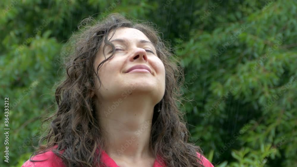 The girl enjoys the summer rain. Looking up at the drops and clouds. In a red cloak. Face. The girl enjoys the summer rain. Looking up at the drops and clouds. In a red cloak. Face.