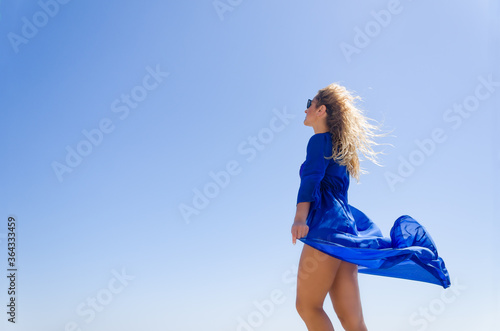 Attractive young woman in blue dress on blue sky background