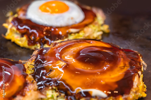Принти на полотні Close-up on a fried egg and an okonomiyaki Japanese omelet prepared with shredded cabbage, cooked on both sides on a hot plate and brushed over in circle with oyster and worcestershire sauce