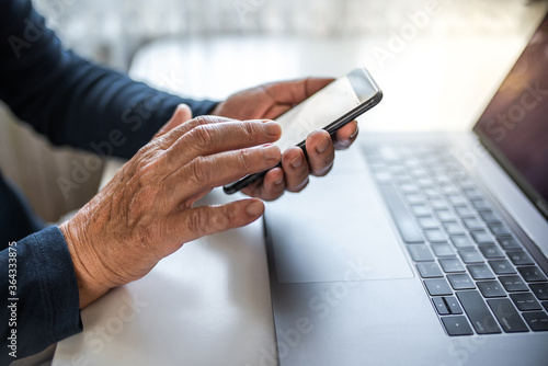 Senior person using mobile phone and laptop at home