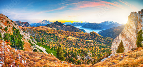 Awesome autumn in Dolomite Alps with larches i and mountaines Marmolada and Monte Civetta at sunset.