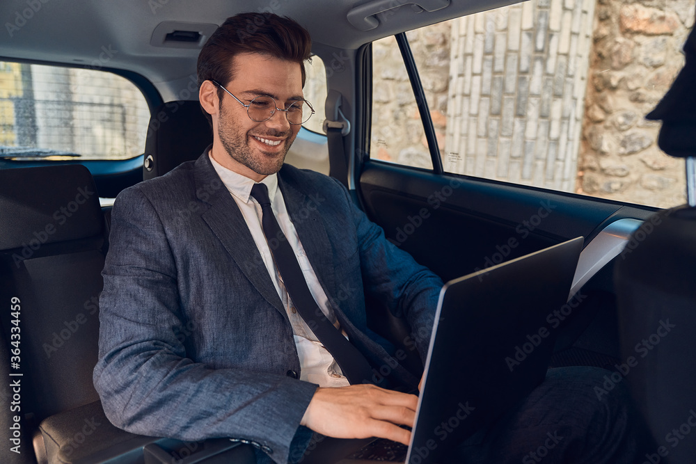 Great solutions every day. Confident young businessman working on his laptop and looking at camera while sitting in the car