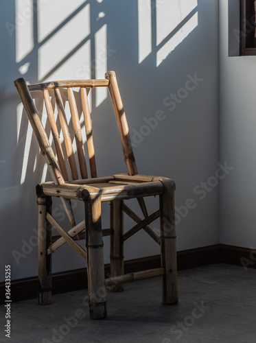 Lonely bamboo chair stands by a window with the sun shining in