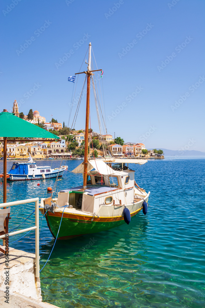 Boat anchoring in beautiful Symi bay with emerald green sea water. Symi island, Greece.
