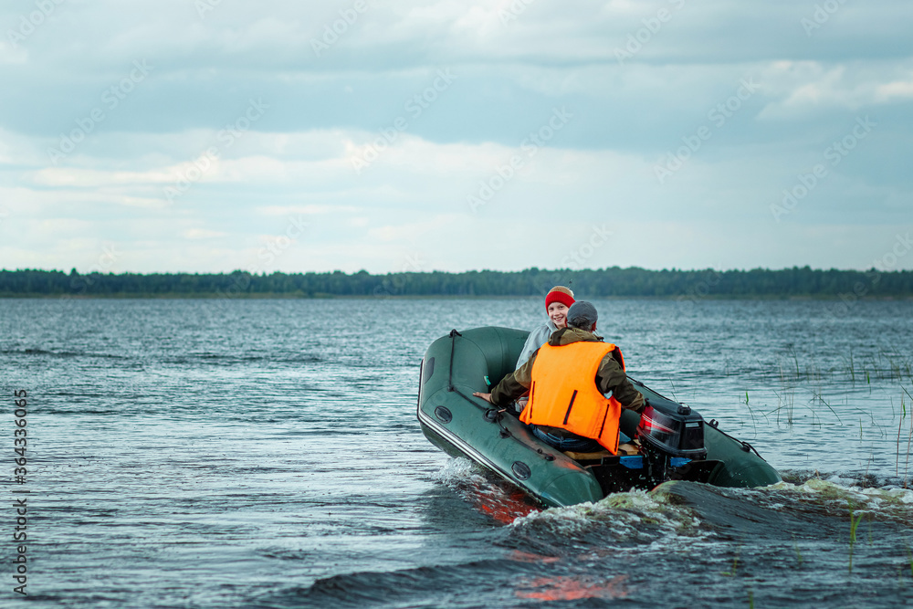 Fototapeta premium Father and son ride a motor boat on the lake. The concept of family, summer vacation, generation. Copy space.