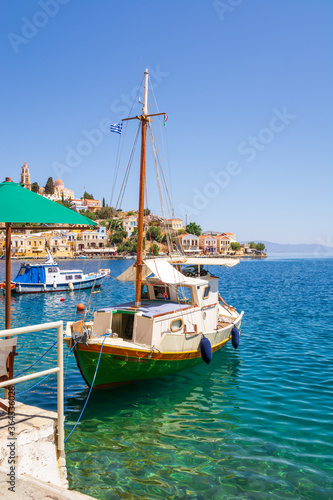 Boat anchoring in beautiful Symi bay with emerald green sea water. Symi island, Greece.