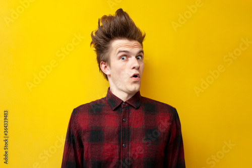 shocked guy surprised at yellow isolated background, hipster with funny hairstyle in shock, close-up
