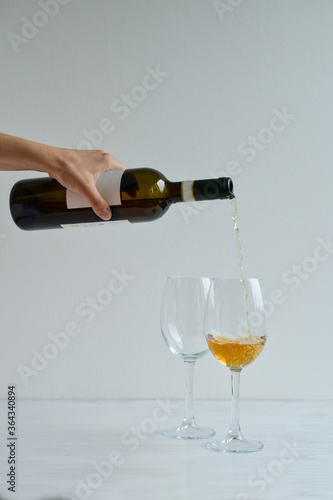 Bottle and two glasses of white wine standing on the white table
