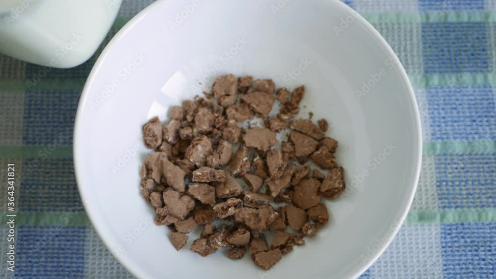 Closeup with a person at breakfast who mixes fresh milk with cereal in a bowl using a spoon Closeup with a person at breakfast who mixes fresh milk with cereal in a bowl using a spoon