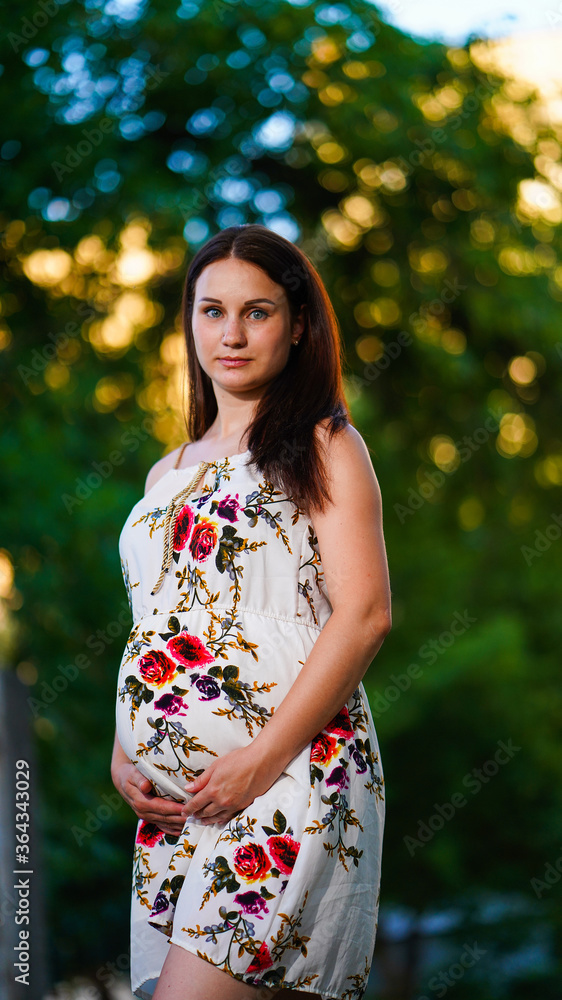 Pregnant mother with long hair posing in summer park.