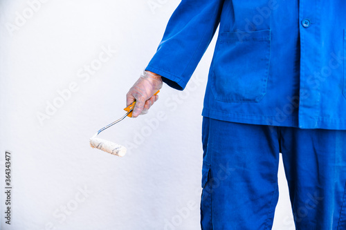 Hand of anonymous painter in a blue uniform holding a paint roller. Closeup view of painter.