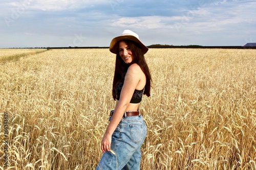 Young happy beautiful slender girl with long hair and a hat in a wheat field. Summer landscape © Helen