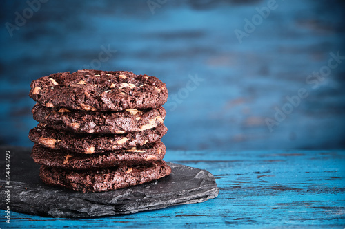 Stack of chokolate cookies with cocoa, chocolate and hazelnuts on blue wooden background.