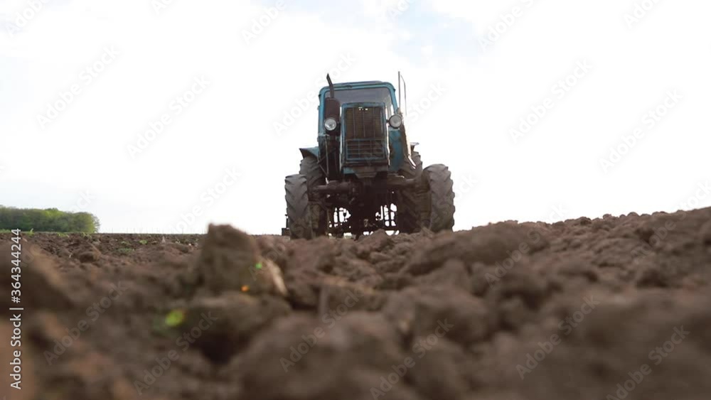Old tractor plowing field, preparing land for sowing, driving over the camera at sunset, bottom view