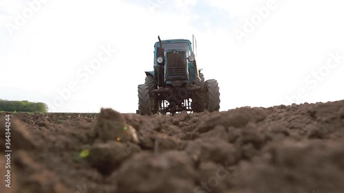 Old tractor plowing field, preparing land for sowing, driving over the camera at sunset, bottom view