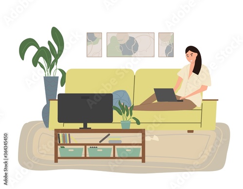 Cute young woman sitting on the couch with laptop computer in cozy room front of the TV.