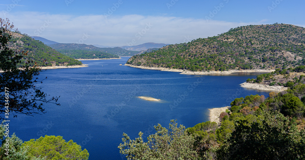 Obraz premium lake panoramic landscape with hills, mountains and small sailboat in the background