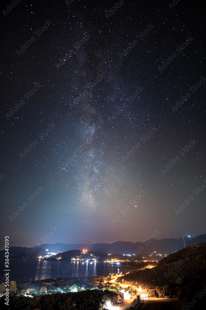 A photo of stars above the sea, with the visible milky way in the background, on the island Sardinia near Villasimius, Italy.