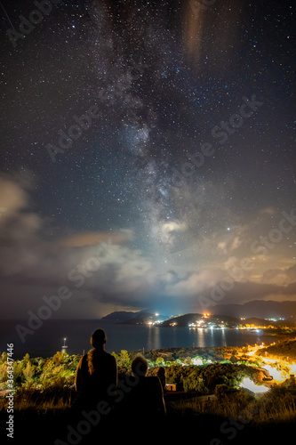 A couple is sitting under the stars, in front of the sea, with the visible milky way in the background, on the island Sardinia near Villasimius, Italy.