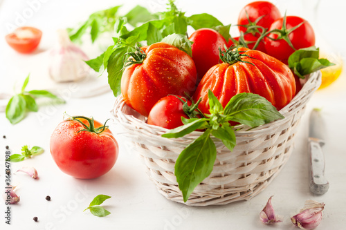 Assorted fresh ripe tomatoes and basil in basket.  Healthy food concept. Clean eating
