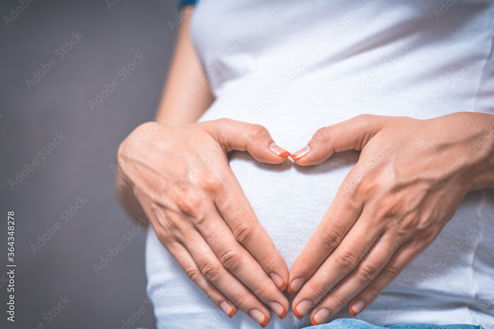 Pregnant Woman holding her hands in a heart shape on her baby bump. Pregnant Belly with fingers Heart symbol. Maternity concept. Toned photo of pregnancy. Pregnant Woman holding her hands in a heart shape on her baby bump. Pregnant Belly with fingers Heart symbol. Maternity concept. Toned photo of pregnancy.