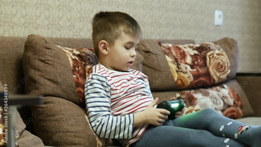Little boy plays in video game with joystick on the couch at home on vacations Little boy plays in video game with joystick on the couch at home on vacations