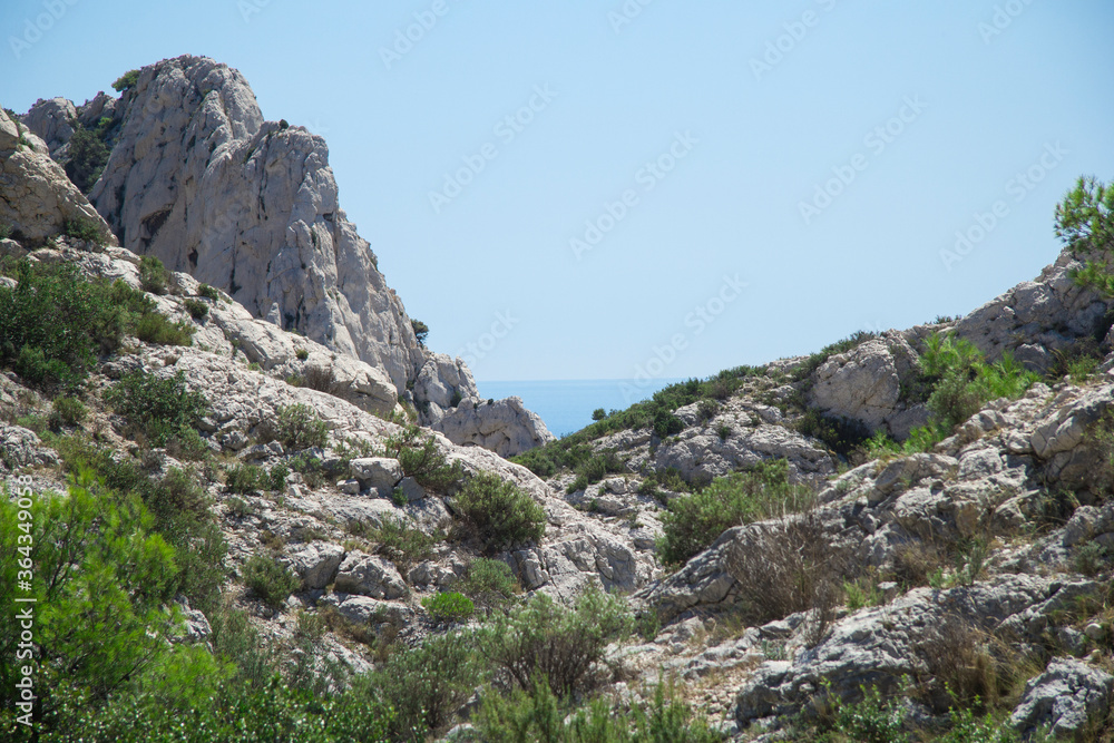 Landscape of mountaint with small rocks and green bushes under the blue sky with the sea in the background in the Calanques de Marseille in France