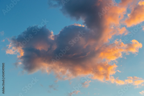 Dramatic golden Cumulus clouds at sunset with bright orange yellow light as sun sets in blue heavenly sky