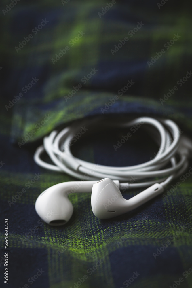 Overhead shot of the wired in-ear white headphones coming out of the chest pocket on the checkered shirt Overhead shot of the wired in-ear white headphones coming out of the chest pocket on the checkered shirt
