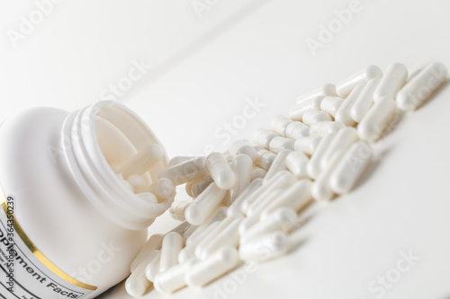 White pills spilled from a toppled white pill bottle on the white background