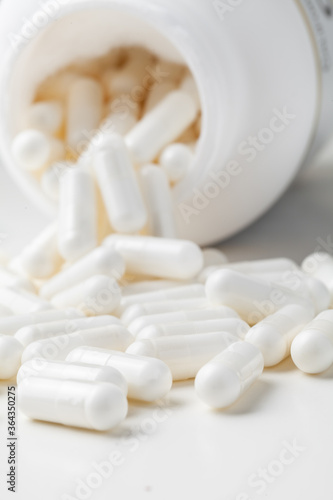 White pills spilled from a toppled white pill bottle on the white background