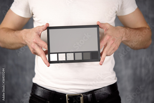 The model holds a color card in its hands for correct color transfer during further color correction. Closeup of a Colorchecker card in the hands. Neutral grey