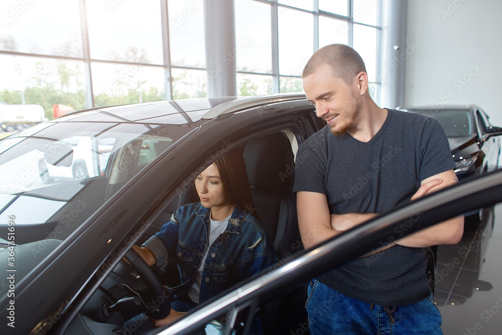 A young couple chooses a new car at a car dealership. Retail car sales A young couple chooses a new car at a car dealership. Retail car sales