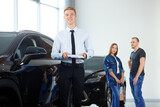 Selective focus Manager of a car dealership showing a luxury car to spouses in a car dealership. The concept of professionalism, the lease agreement, car rental, retail sales