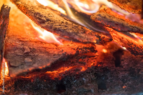 Flame incinerates firewood and transforms it ashes, close up, shallow depth of field. Blaze in a large stove. Nature texture of fire. The flame of fire burns in the brazier, smoldering firewoods.