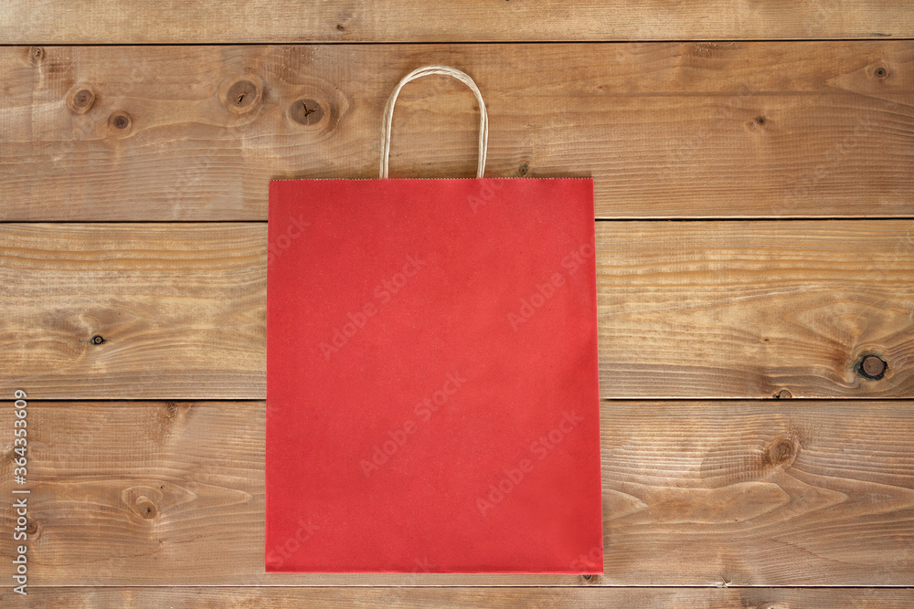 Red paper craft bag on wooden background. Centre composition with empty spot for text. Responsive design mockup. Flat lay, top view. Recycled paper shopping bag with copy space. Eco shopping concept. Red paper craft bag on wooden background. Centre composition with empty spot for text. Responsive design mockup. Flat lay, top view. Recycled paper shopping bag with copy space. Eco shopping concept.