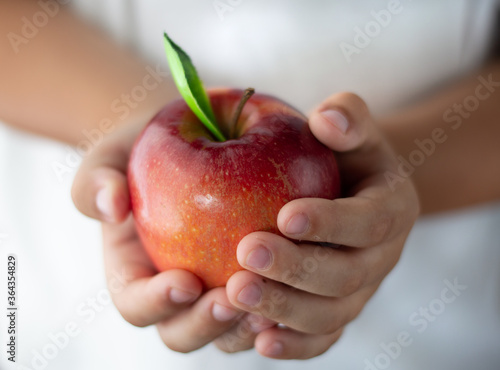 Ripe, red, juicy apple with a leaf in the hands of a child.