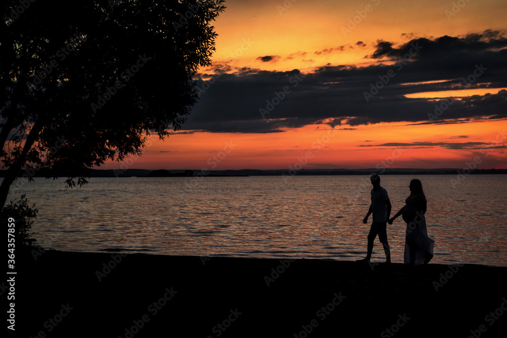 Happy pregnant family walks along the lake in summer sunset Happy pregnant family walks along the lake in summer sunset