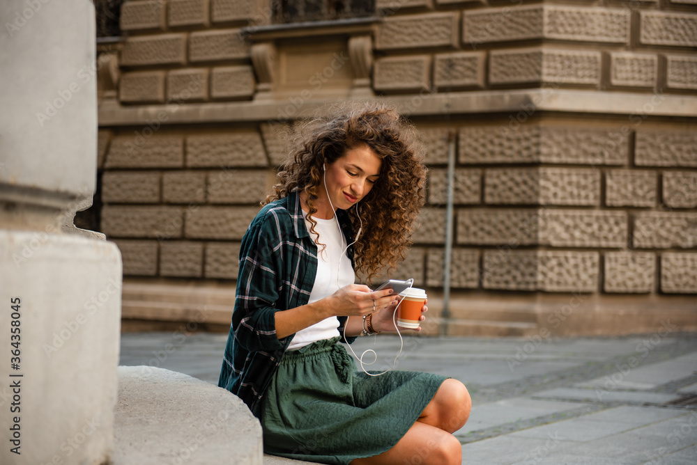 Fototapeta premium Young woman sitting and looking at her smart phone