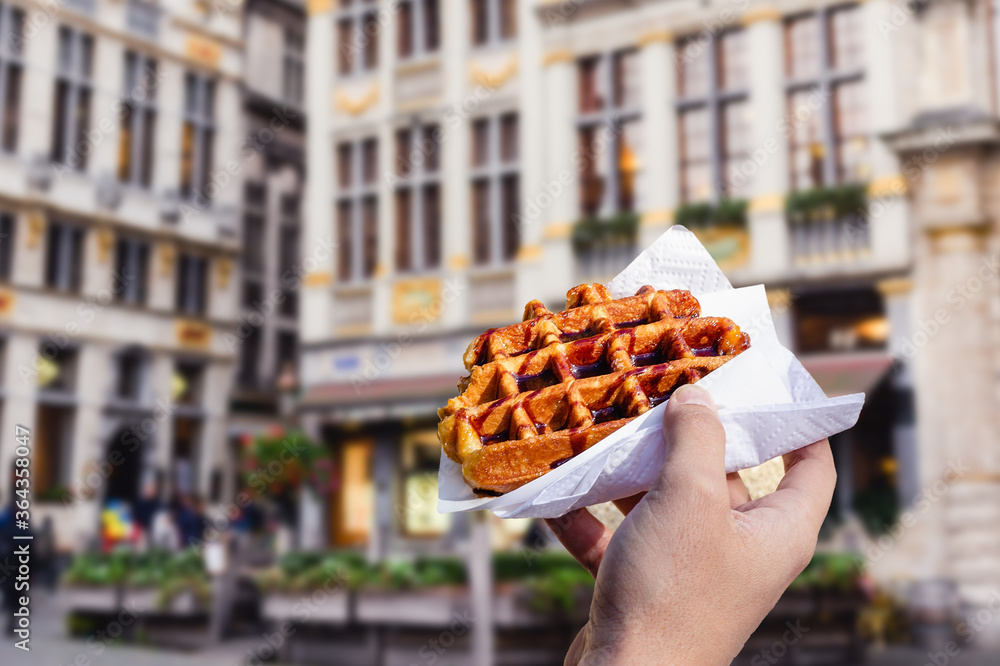 Fototapeta premium Man holds waffle with chocolate sauce on the background of city