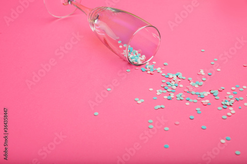 Champagne glass poured out colorful confetti on pink background. Top view. Flat lay. Free space for text.