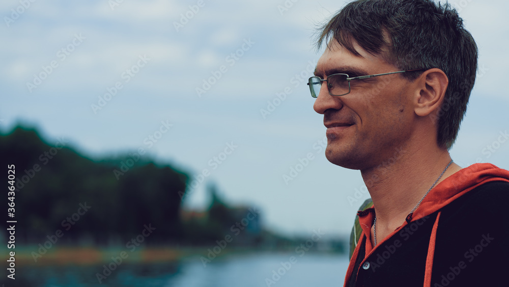 Mature man with glasses standing on embankment. Adult male enjoying walk around city.