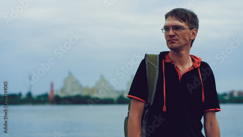 Mature man with glasses standing on embankment. Adult male enjoying walk around city. © Anton Dios