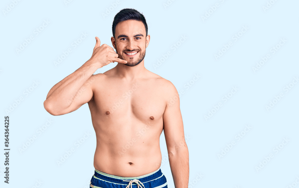 Young handsome man wearing swimwear smiling doing phone gesture with hand and fingers like talking on the telephone. communicating concepts. Young handsome man wearing swimwear smiling doing phone gesture with hand and fingers like talking on the telephone. communicating concepts.